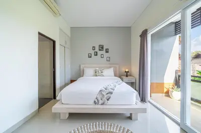 a white bedroom with a bed and a window at De Gani in Seminyak