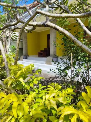 a building with a yellow wall and some trees at Berlian Inn Kuta Beach in Kuta