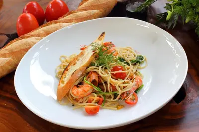 a white plate of pasta with shrimp and a sandwich at Agata Villas Seminyak in Seminyak