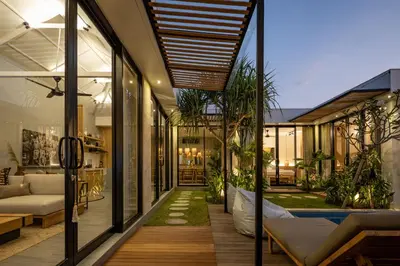 a home with glass walls and a porch with a couch at Ananda Villa by Betterplace in Jimbaran