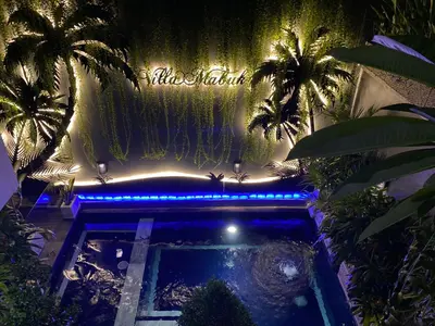 a swimming pool with palm trees and a sign at Villa Mabuk in Legian