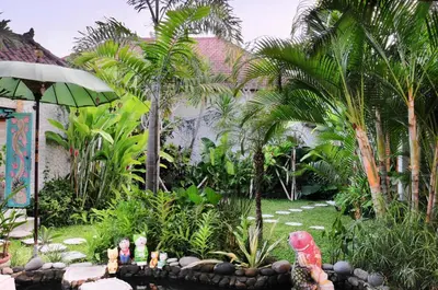 a garden with palm trees and a garden with statues at Villa Domus De Janas in Seminyak