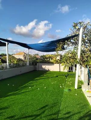 a backyard with green grass and a blue canopy at The Island Bali in Seminyak