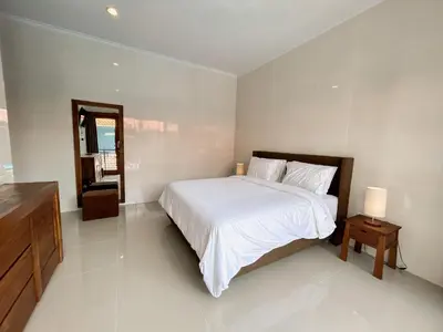 a bedroom with a large white bed and a mirror at James Guest House in Seminyak