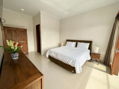 a white bedroom with a bed and a vase of flowers at James Guest House in Seminyak