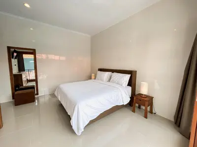 a white bedroom with a bed and a mirror at James Guest House in Seminyak
