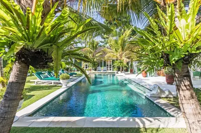 a pool with palm trees in a backyard at Pineapple Hill 4 Bed Luxury in Seminyak