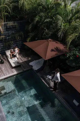 a group of people sitting under an umbrella next to a pool at Black Villas Canggu Beach by OXO in Canggu