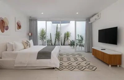 a white bedroom with a large bed and a flat screen tv at Villa Weiss Berawa in Canggu