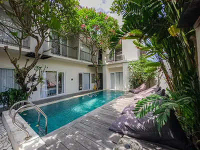 a swimming pool in front of a building with trees at Hola Seminyak in Seminyak