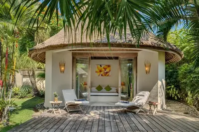 a resort with a thatched roof and chairs on a patio at The Tirta Naga Villas in Seminyak