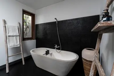 a white bath tub in a bathroom with black tiles at Villa Alopa 1 in Seminyak