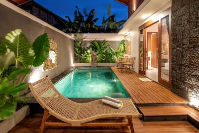 a swimming pool with a deck and chairs and a table at Pondok Arya Kuta Villas by Kamara in Kuta