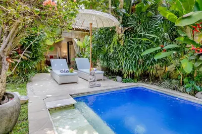 a pool in a garden with two chairs and an umbrella at Villa Balissima in Seminyak