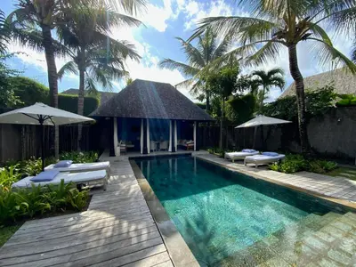 a swimming pool with chairs and umbrellas in a backyard at Villa Samuan in Seminyak