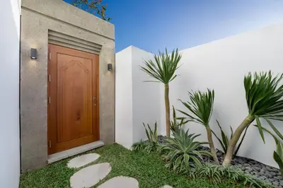 a wooden door on the side of a house with palm trees at Villa ElyOs Canggu by Nagisa Bali in Canggu