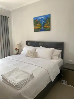 a bed with white sheets and a painting on the wall at Queen’s Villa in Seminyak