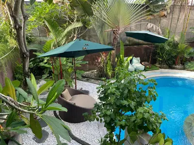 a garden with a pool and umbrella and plants at Umah Kita Villa in Seminyak