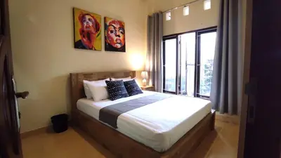 a bedroom with a bed and a large window at Moara Guest House in Kerobokan