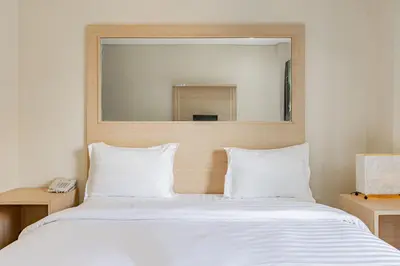 a bedroom with a large white bed with a mirror at Collection O Kuta Near Airport Ngurah Rai in Kuta