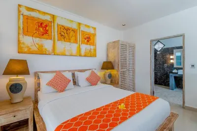 a bedroom with a large bed with an orange blanket at Villa Rama Sita - 100m from Eat Street, 3BR in Seminyak