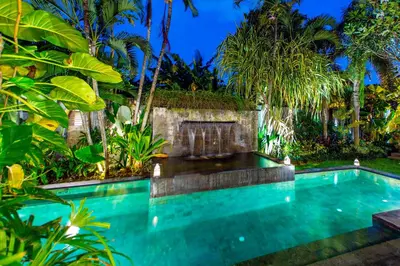 a swimming pool in a garden with palm trees at Villa Taksu Legian in Legian