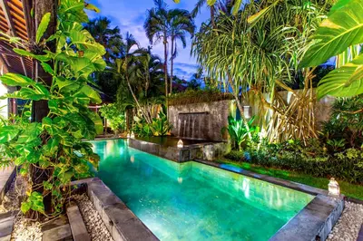 a swimming pool in a garden with palm trees at Villa Taksu Legian in Legian