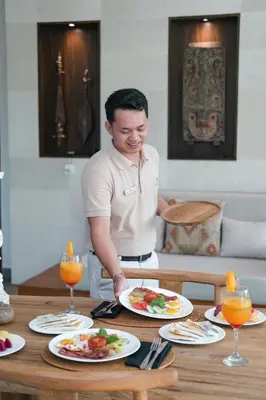 a man standing in front of a table with plates of food at Kerta Rama Seminyak by Kerta Living in Seminyak