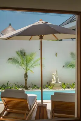 a patio with an umbrella and chairs and a pool at Villa Umaju - Contemporary Minimalist 2BR Villa in Umalas! in Canggu