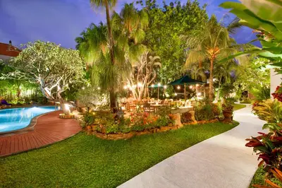 a resort yard with a swimming pool and palm trees at Astagina Resort Villa and Spa in Legian