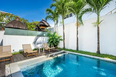 a swimming pool with two chairs and a table and palm trees at Villa Oberoi in Seminyak
