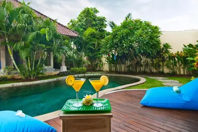 a table with two glasses on it next to a swimming pool at Villa Domus Dua in Seminyak