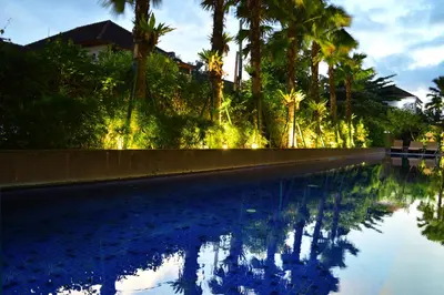 a swimming pool with palm trees and lights at HARRIS Hotel Seminyak in Seminyak