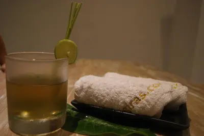 a glass of drink next to a towel and a lime at Sugiras Living in Denpasar