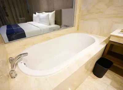 a bathroom with a tub and a bed in a mirror at Platinum Hotel Jimbaran Beach Bali in Jimbaran