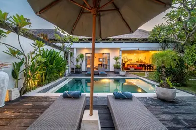 a swimming pool with an umbrella and benches next to a house at Villa Ricci Seminyak in Kerobokan