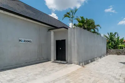 a white building with a black door and palm trees at Villa KALOOKA, a vacation in paradise. in Seminyak