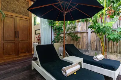 a porch with two chairs and an umbrella at The Gardens Seminyak in Seminyak
