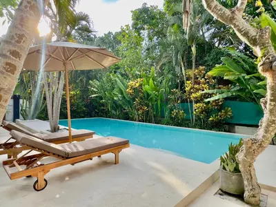 an umbrella and a lounge chair next to a swimming pool at An Amazing 6BDR Private Family Villa with Pool in Tanah Lot