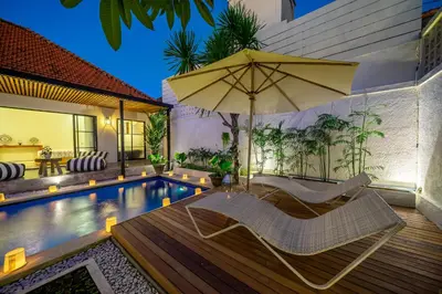 an umbrella and chairs next to a swimming pool at Kalya Villa by RPM in Seminyak