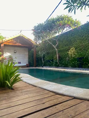 a swimming pool with a wooden deck next to a house at Meilds Property Segara Kuta in Kuta