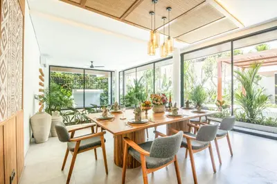 a dining room with a wooden table and chairs and large windows at Brand new Luxury 5 br villa 200m to Brawah Beach in Canggu