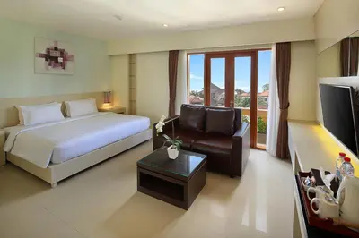 a bedroom with a bed and a couch and a television at Bali Chaya Hotel Legian in Legian