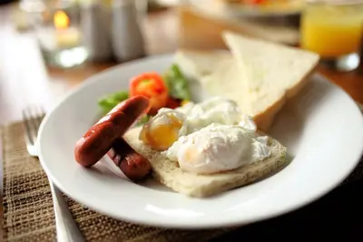 a plate of food with sausage eggs and bread at Paragon Hotel Seminyak in Seminyak