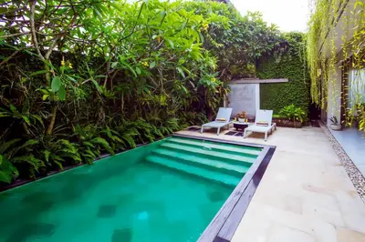 a swimming pool in a backyard with two chairs and trees at Villa Casabola - Seminyak in Seminyak
