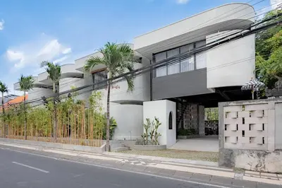 a white building with palm trees in front of a street at Town House CAMY in Seminyak