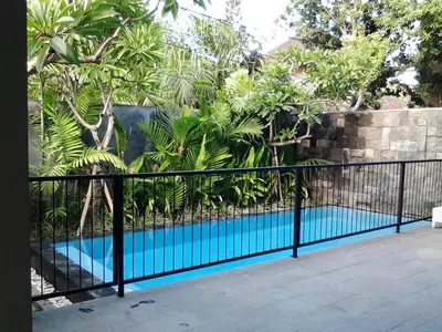 a fence with a blue swimming pool in front of a wall at Abivilla in Seminyak