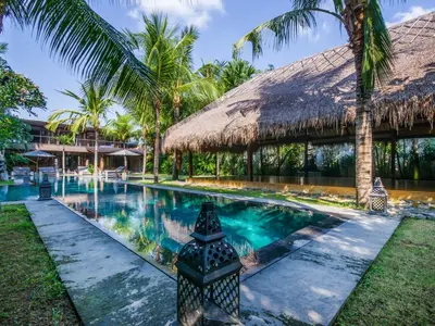 a swimming pool in front of a resort with palm trees at Villa Yoga by Villa Finder in Seminyak