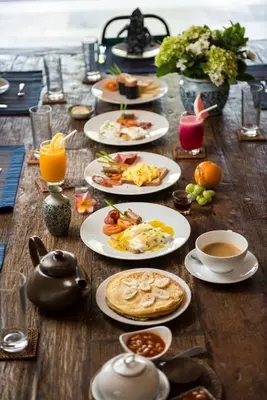 a wooden table with plates of breakfast food on it at Villa Tiga Puluh, 7 Bedrooms Private Villa in Seminyak in Seminyak