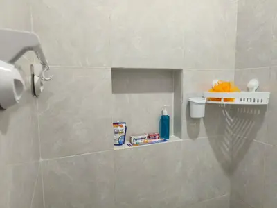 a tiled bathroom with a shelf with cleaning products on it at Justin Guest House in Jimbaran